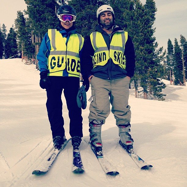 Noah standing on skis beside an adaptive ski guide on a snowy mountain